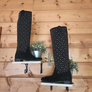 May include: A pair of black knee-high boots featuring a dense pattern of small silver-toned metal studs covering the entire shaft. The boots have a rounded toe, a flat heel, and a pull tab at the top of the shaft, constructed from a soft material.