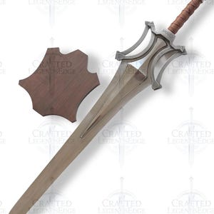 May include: A silver-colored sword with a brown leather-wrapped handle and a matching wooden shield. The sword has a long, double-edged blade and ornate crossguard. The shield is a dark brown, irregular shape.