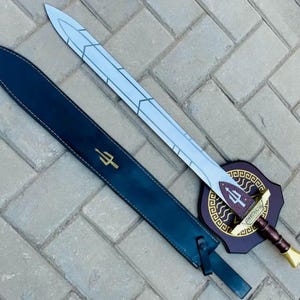 May include: A decorative sword with a silver blade and a brown handle, resting on a wooden plaque with a trident symbol. The sword is accompanied by a black sheath with a gold trident emblem.