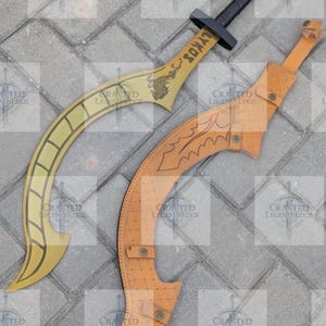 May include: Two curved swords with tan blades and black handles. One sword has the word "LYKOS" on the blade. The other sword is in a tan leather sheath with decorative etching. The swords are displayed on a gray stone surface.