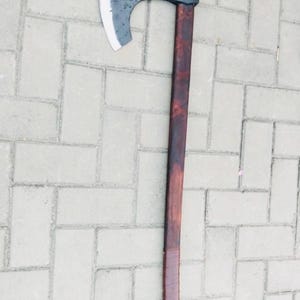 May include: A large axe with a dark metal blade and a long, dark wooden handle. The axe head has a curved blade with a sharp edge. The handle is a rich, dark brown color. The axe is designed for chopping or splitting wood.