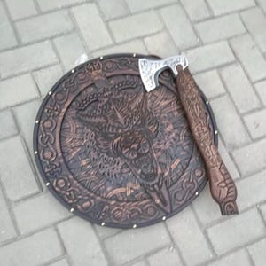 May include: A round, wooden shield with a carved wolf design and intricate patterns. A matching wooden axe with a silver blade rests on the shield. The shield is approximately 24 inches in diameter.