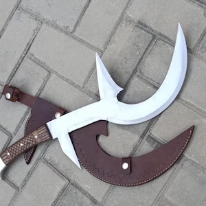 Könnte beinhalten: Eine große, gebogene Klinge mit weißer Oberfläche und einem braunen Holzgriff. Die Klinge ist mit einer braunen Lederscheide kombiniert. Der Griff hat ein detailliertes, strukturiertes Muster. Das Gesamtdesign deutet auf eine Waffe oder einen Dekorationsgegenstand hin.