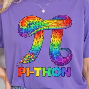 May include: Purple t-shirt featuring a colorful graphic of a snake coiled around the mathematical symbol Pi. The snake is designed in rainbow colors, with the text "PI-THON" in a rainbow gradient below the graphic.