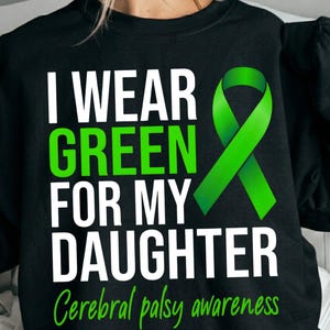 Op de afbeelding: Zwart sweatshirt met de tekst "I WEAR GREEN FOR MY DAUGHTER" in wit en groen. Een groene lintafbeelding staat rechts. De woorden "Cerebral palsy awareness" staan in het groen onderaan.