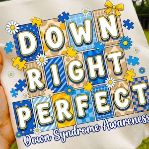 May include: Cream-coloured t-shirt with the words "DOWN RIGHT PERFECT" in large, colourful letters. The design includes puzzle pieces, daisies, and a yellow bow, with "Down Syndrome Awareness" written below.