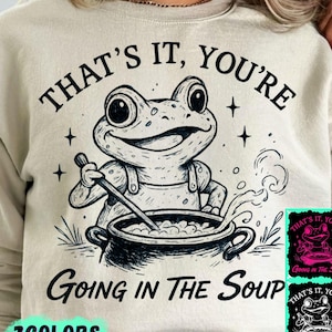 May include: Beige sweatshirt with a graphic of a frog stirring a pot of soup. The text "THAT'S IT, YOU'RE GOING IN THE SOUP" is above and below the frog illustration. The words "3 COLORS" are at the bottom.