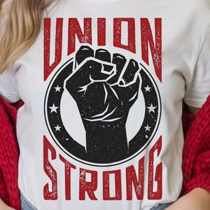 May include: White t-shirt with a distressed red "UNION STRONG" graphic. The design features a black fist inside a black circle with white stars. The shirt is made of a soft material.