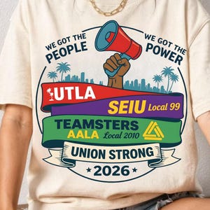 May include: A cream-coloured t-shirt with a graphic design. The design features a megaphone held by a brown hand, and the text "WE GOT THE PEOPLE" and "WE GOT THE POWER". The design includes the text "UTLA", "SEIU Local 99", "TEAMSTERS AALA Local 2010", "UNION STRONG", and "2026".