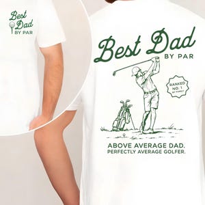 Op de afbeelding: Een wit t-shirt met groene afbeeldingen. De voorkant toont een golfbal op een tee met de tekst "Best Dad BY PAR". De achterkant toont een golfer, een golftas en de tekst "Best Dad BY PAR", "RANKED NO. 1 BY FAMILY" en "ABOVE AVERAGE DAD. PERFECTLY AVERAGE GOLFER."