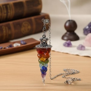 Op de afbeelding: Een chakra-pendel met een zilveren ketting en een veelkleurig kristallen ontwerp. De pendel heeft een spiraal van rode, oranje, gele, groene, blauwe, indigo en violette stenen. De pendel wordt gebruikt voor spirituele praktijken.
