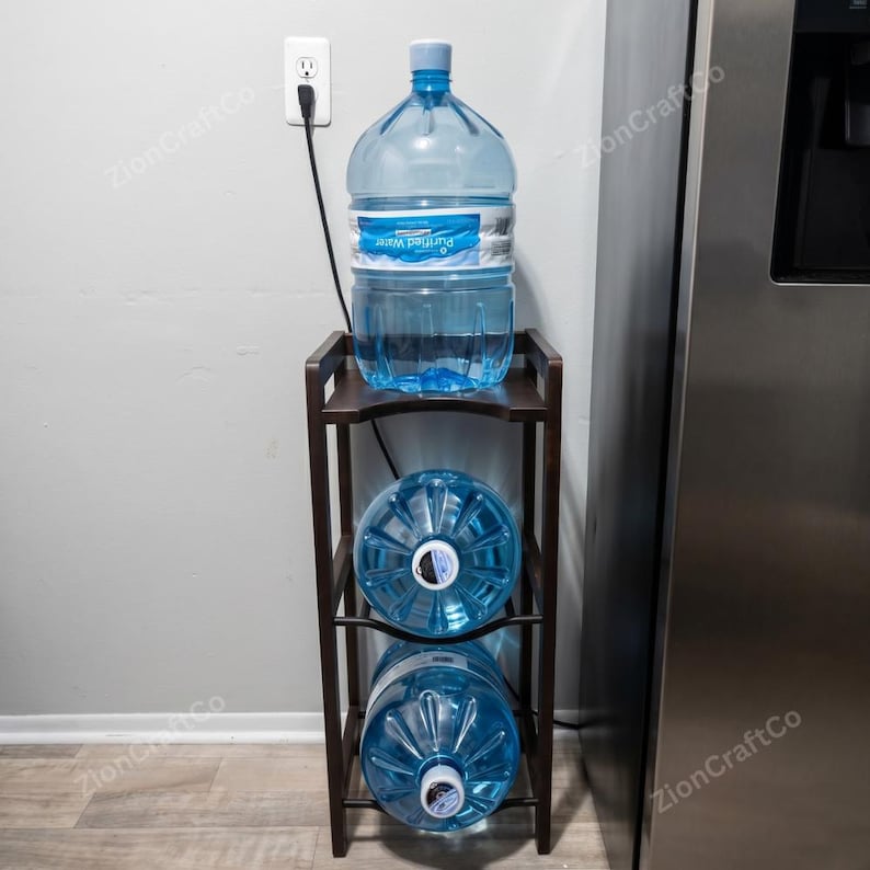 May include: A dark brown wooden water jug storage rack with three tiers. The top tier holds one large clear plastic water jug upright, while the middle and bottom tiers each hold one large clear plastic water jug positioned on its side.