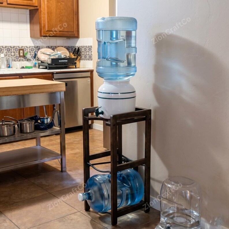May include: A dark brown wooden water cooler stand with a rectangular frame and a lower shelf. A white water dispenser with a large clear plastic jug sits on top, while a second clear plastic water jug rests horizontally on the bottom shelf.