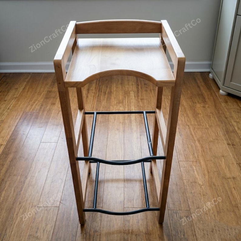 May include: A tall wooden stool featuring a light brown natural wood finish, a curved seat, and a sturdy frame. The structure includes two horizontal black metal support bars connecting the four legs, providing stability for this piece of furniture.
