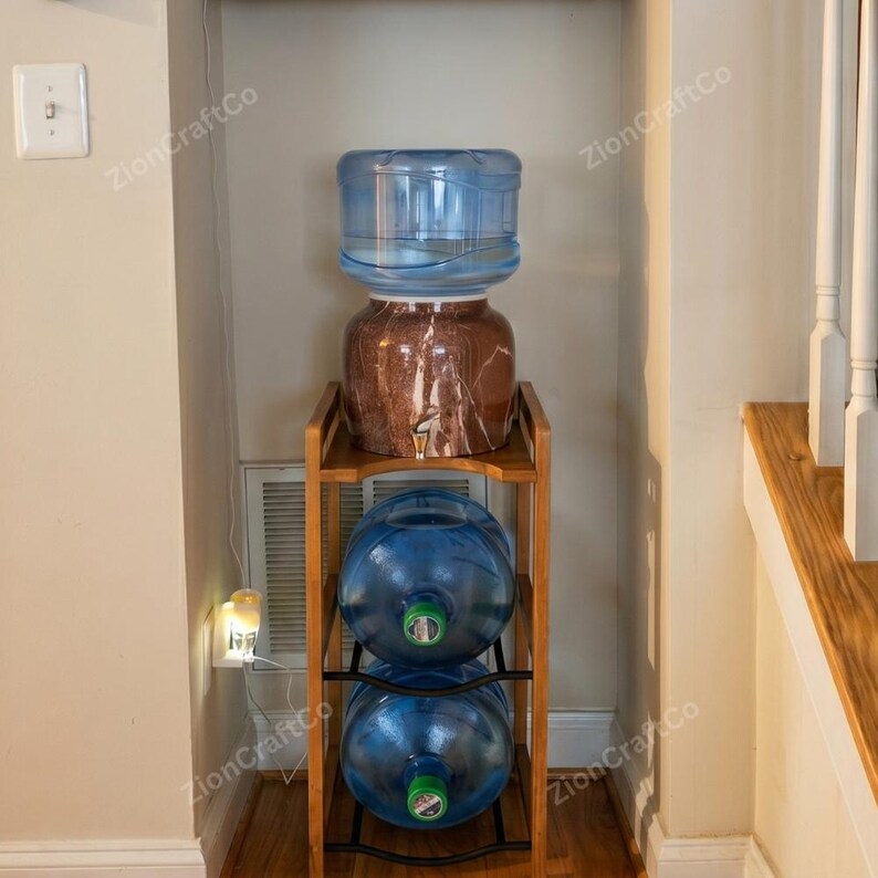 May include: A three-tier wooden stand holding two large blue plastic water jugs on the bottom shelves and a brown marble-patterned water dispenser with a clear plastic water bottle on the top shelf, featuring a metal spigot for dispensing water.