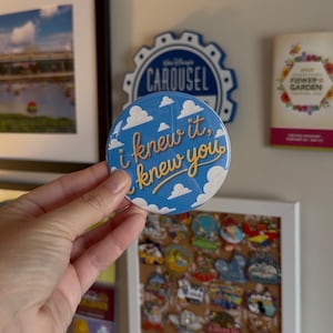May include: A circular button with a blue background featuring white clouds and the yellow cursive text "i knew it, knew you". The design is inspired by the iconic wallpaper pattern from the film Toy Story, showcasing a bright and clear graphic.