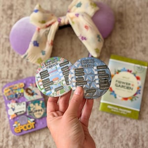 May include: A collection of Disney-themed merchandise, including purple mouse ears with a floral bow, two round pins with "Drinking Around the World" text, a pin board, and a "Flower & Garden" booklet.