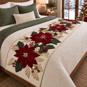May include: A cream-colored quilted bed runner featuring a decorative arrangement of red poinsettia flowers, dark green leaves, gold-toned foliage, brown pinecones, small white berries, and gold ornaments centered along the length of the fabric.