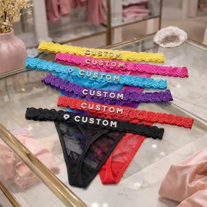 Puede incluir: Una colección de tangas de colores con adornos de encaje y la palabra "CUSTOM" con pedrería. Los tangas son de varios colores, incluyendo amarillo, rosa, azul, morado, rojo y negro.