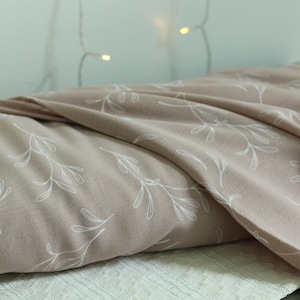 May include: A roll of dusty rose fabric featuring a repeating white line-art pattern of delicate leafy branches. The textile is draped in soft folds, showcasing the smooth texture and the consistent botanical print across the surface of the material.