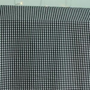 Op de afbeelding: Een rol stof met een klassiek zwart-wit gingham ruitpatroon. Het textiel vertoont een consistent, herhalend raster van kleine, afwisselende vierkantjes over het gehele oppervlak, wat een contrastrijk, uniform geometrisch ontwerp cre&euml;ert.