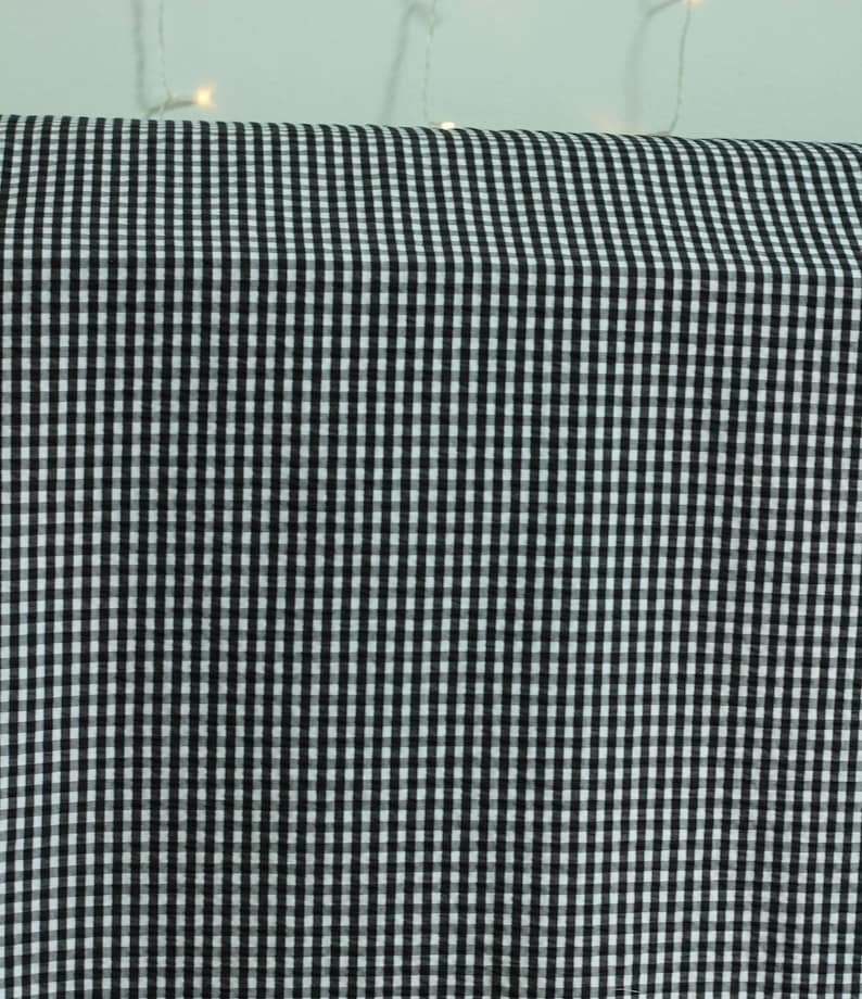 Op de afbeelding: Een rol stof met een klassiek zwart-wit gingham ruitpatroon. Het textiel vertoont een consistent, herhalend raster van kleine, afwisselende vierkantjes over het gehele oppervlak, wat een contrastrijk, uniform geometrisch ontwerp cre&euml;ert.