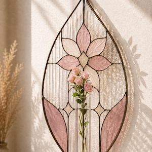 May include: A leaf-shaped stained glass wall hanging featuring a metal frame with clear textured glass and pink glass petals. A central clear glass tube holds a small bouquet of light pink roses. The piece includes a metal ring for hanging.
