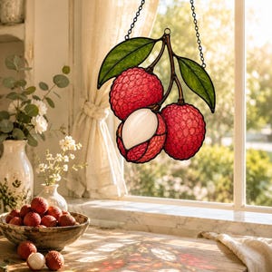 May include: A stained glass suncatcher featuring three lychee fruits hanging from a branch with green leaves. Two fruits are textured red with bumpy skins, while the third is partially peeled to reveal a smooth, white, translucent interior.