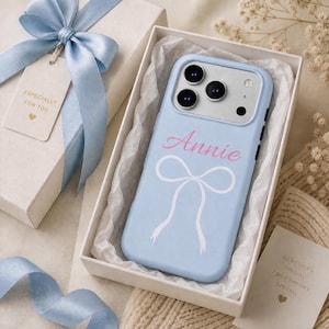 May include: A light blue phone case with the name "Annie" in pink script and a white bow design. The case is in a white gift box with tissue paper. A gift tag with a blue ribbon reads "Especially for you."