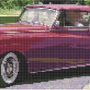 May include: A classic burgundy convertible car with white-walled tires. The car has a chrome grill and headlights. The top is down, and the car is parked on a street with a green background.