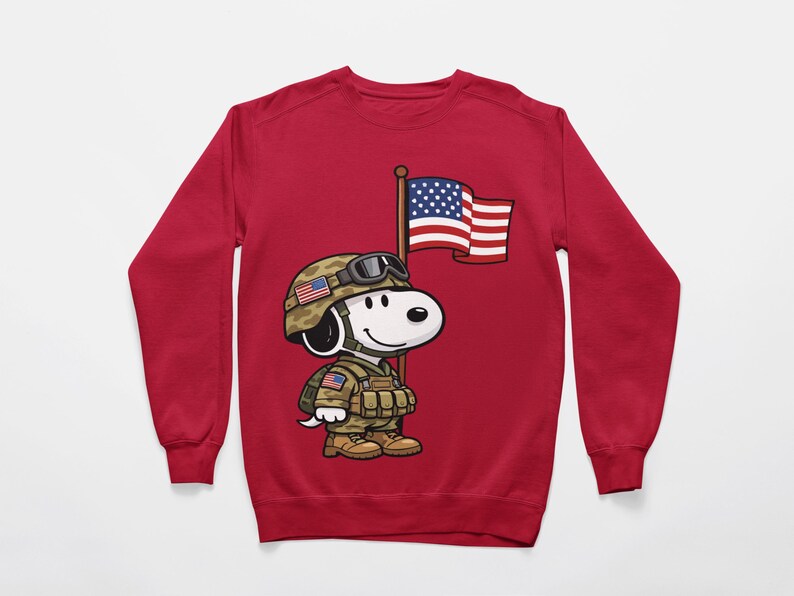 May include: A red sweatshirt featuring a cartoon character in military attire, complete with a helmet, uniform, and an American flag. The character is holding a flagpole with the American flag. The design is centered on the front of the sweatshirt.