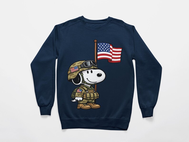 May include: Navy blue sweatshirt featuring a cartoon Snoopy character dressed as a soldier, wearing a helmet with an American flag design. Snoopy is holding a flagpole with the American flag. The design is centered on the front of the sweatshirt.