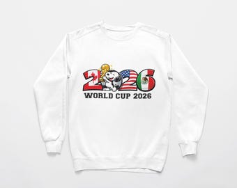 Może przedstawiać: Biała bluza z napisem "2026 WORLD CUP". Cyfry zaprojektowano jako flagi Kanady, Stanów Zjednoczonych i Meksyku. Postać z kreskówki trzyma trofeum Pucharu Świata. Zabawny design dla fanów piłki nożnej.