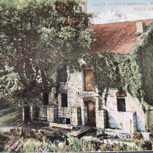 May include: Vintage postcard featuring the Old Commissary, built in 1830, in Fort Smith, Arkansas. The image shows a stone building with a red roof, partially covered in ivy, and surrounded by trees. The postcard has a faded, aged appearance.