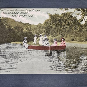May include: Vintage postcard depicting a group of people boating on the Bourbeuse River at Horseshoe Bend near Union, Missouri. The postcard shows a red boat with several people wearing hats, surrounded by water and trees. The text "Boating on Bourbeuse River Horseshoe Bend near Union, Mo." is visible.