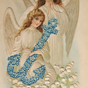 May include: Vintage Easter greeting card featuring two angels with wings. One angel holds a blue floral anchor, while the other has hands clasped in prayer. White lily of the valley flowers are at the bottom, with the words "EASTER GREETING".