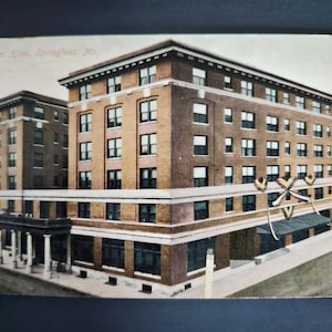 May include: Vintage postcard featuring the Colonial Hotel in Springfield, Missouri. The multi-story building is constructed of brick and features numerous windows. The postcard has a faded appearance, suggesting its age.