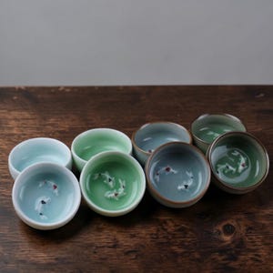 Puede incluir: Un juego de tres tazas de cerámica con un acabado mate moteado. Las tazas son en tonos crema, gris claro y gris oscuro. Cada taza tiene un diseño simple y minimalista, ideal para café o té.