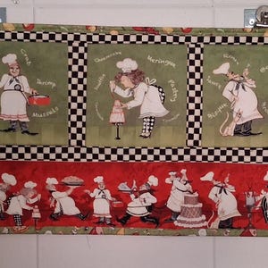 May include: A rectangular kitchen wall hanging featuring cartoon chefs. The top section has four green squares with chef illustrations and text. The bottom section has a red background with more chef illustrations. The border has a black and white checkered pattern.