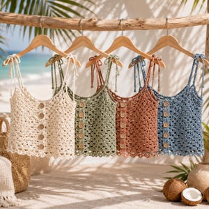 May include: Four sleeveless crochet camisoles hanging on wooden hangers. Each top features a square neckline, thin tie-up shoulder straps, and a vertical row of five round wooden buttons down the centre. The colours are cream, sage green, terracotta, and blue.