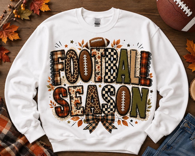 May include: A white long-sleeve sweatshirt featuring the text FOOTBALL SEASON in large, multi-patterned letters. The design includes plaid, leopard print, and checkered textures, accented with football illustrations, autumn leaves, and a bow.