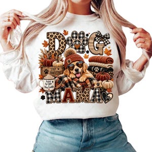 Puede incluir: Una sudadera blanca de manga larga con un estampado gr&aacute;fico de un golden retriever con gafas de sol en forma de coraz&oacute;n y un gorro. El dise&ntilde;o incluye hojas de oto&ntilde;o, calabazas, una taza con la inscripci&oacute;n "Fueled by Coffee Dog Cuddler" y el texto "DOG MAMA".