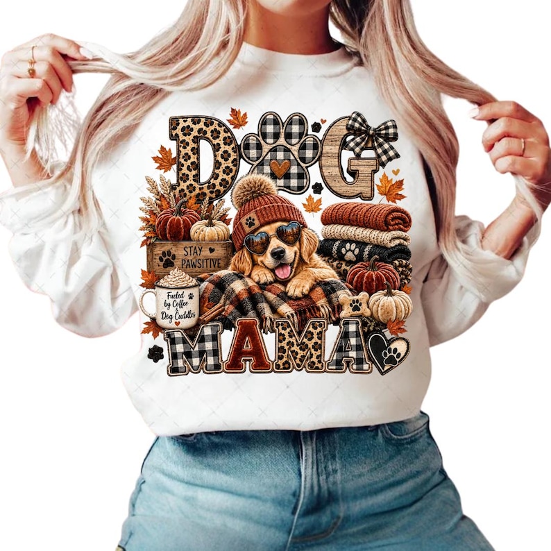 Puede incluir: Una sudadera blanca de manga larga con un estampado gr&aacute;fico de un golden retriever con gafas de sol en forma de coraz&oacute;n y un gorro. El dise&ntilde;o incluye hojas de oto&ntilde;o, calabazas, una taza con la inscripci&oacute;n "Fueled by Coffee Dog Cuddler" y el texto "DOG MAMA".