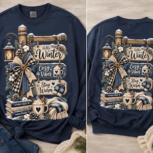 May include: A navy blue long-sleeve sweatshirt featuring a graphic print of a wooden signpost with three hanging signs that read Hello Winter, Cozy Vibes, and Stay Warm. The design includes a lantern, a plaid bow, pinecones, books, and a mug.
