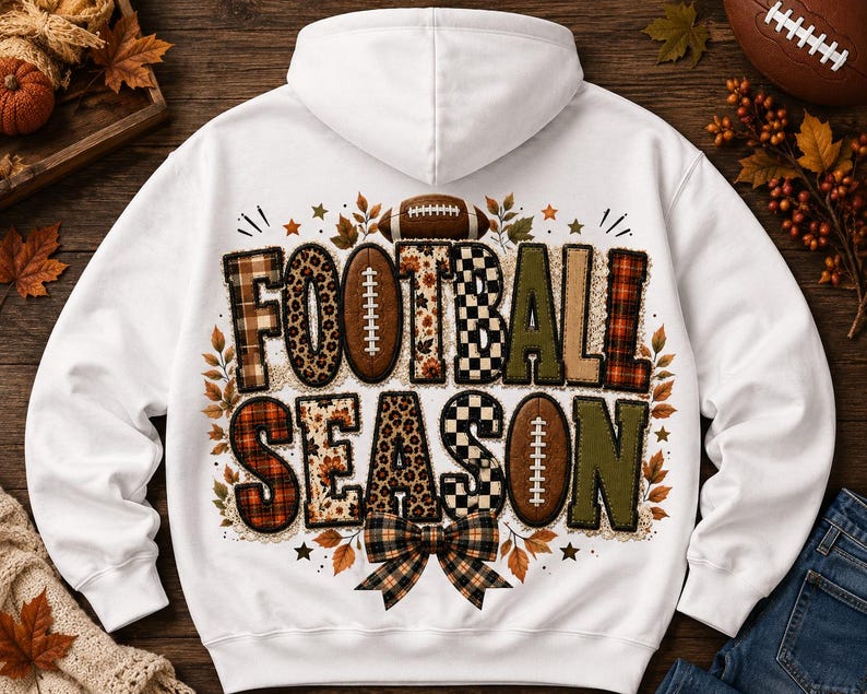 May include: A white hooded sweatshirt featuring a graphic on the back with the text FOOTBALL SEASON. The letters are filled with various patterns including leopard print, plaid, and checkered designs, accented by footballs and autumn leaves.