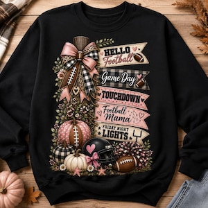May include: A black sweatshirt featuring a graphic print of a football-themed design with pumpkins, a helmet, a bow, and banners reading Hello Football, Game Day, TOUCHDOWN, Football Mama, and FRIDAY NIGHT LIGHTS with various football icons.