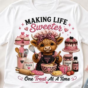May include: A white t-shirt featuring a graphic of a fluffy brown cow wearing a pink leopard print chef hat and apron. The text reads "MAKING LIFE Sweeter" and "One Treat At A Time". The cow is surrounded by baking items like cupcakes, a cake, flour, sugar, and vanilla extract.