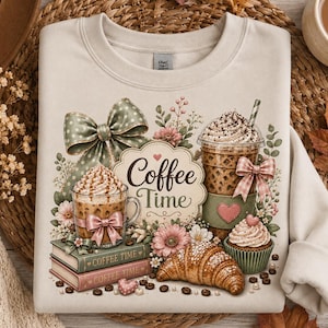 Puede incluir: Una sudadera de cuello redondo en color beige con un estampado gráfico de una taza de café, un café helado, un cruasán, un cupcake y dos libros etiquetados como Coffee Time. El diseño incluye un lazo verde grande, flores rosas y granos de café.