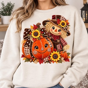 Pode incluir: Uma camisola de gola redonda cor de creme com uma impressão gráfica de uma abóbora sorridente com um laço castanho às bolinhas e um girassol, ao lado de um espantalho com chapéu xadrez e jardineiras, rodeado por folhas de outono e abóboras.