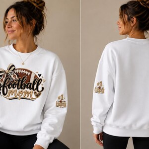 Peut inclure: Un sweat-shirt blanc &agrave; col rond avec un motif sur le devant repr&eacute;sentant un ballon de football marron, un n&oelig;ud &agrave; carreaux noir et blanc et le texte "football mom" en &eacute;criture noire. La manche porte le motif "#1 CHEER" avec un petit ballon.